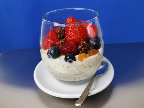 Hermosa imagen de un vaso de cristal lleno de kéfir y mezclado con frutas y granola. Salud y sanación de adentro hacia afuera.